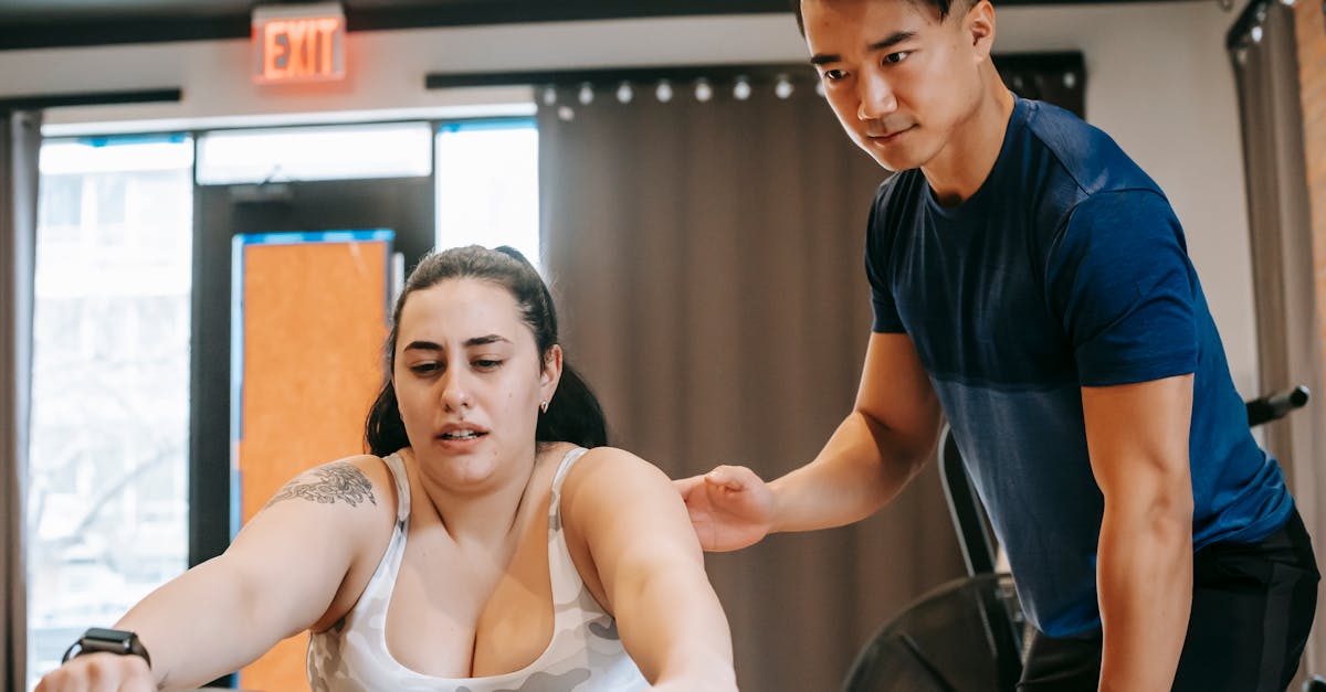 young handsome ethnic experienced trainer supporting plus size woman working out on rowing machine i
